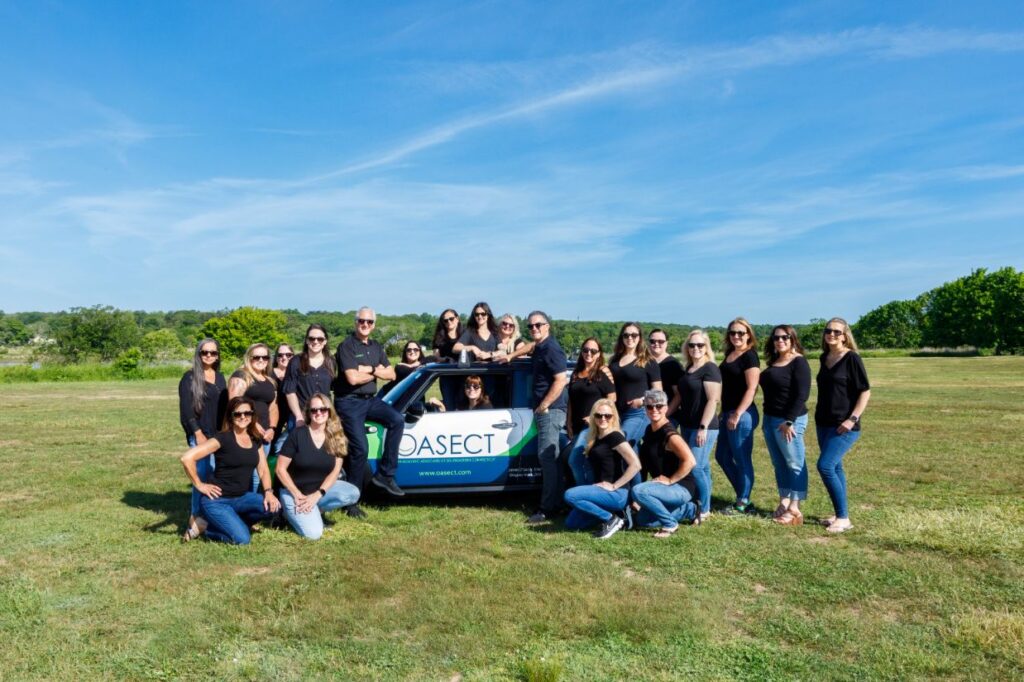 OASECT team posing around the OASECT car in a large green field