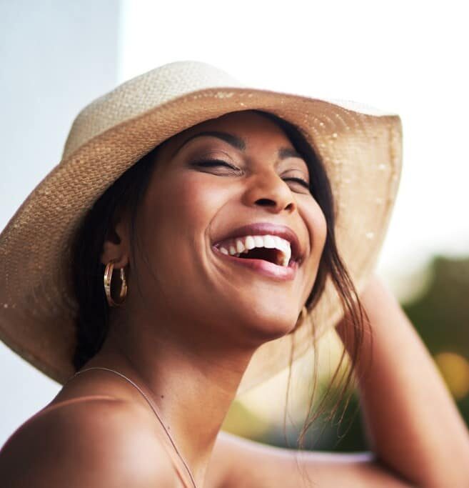 Stunning woman with disarming smile lauging while holding her hat onto her head