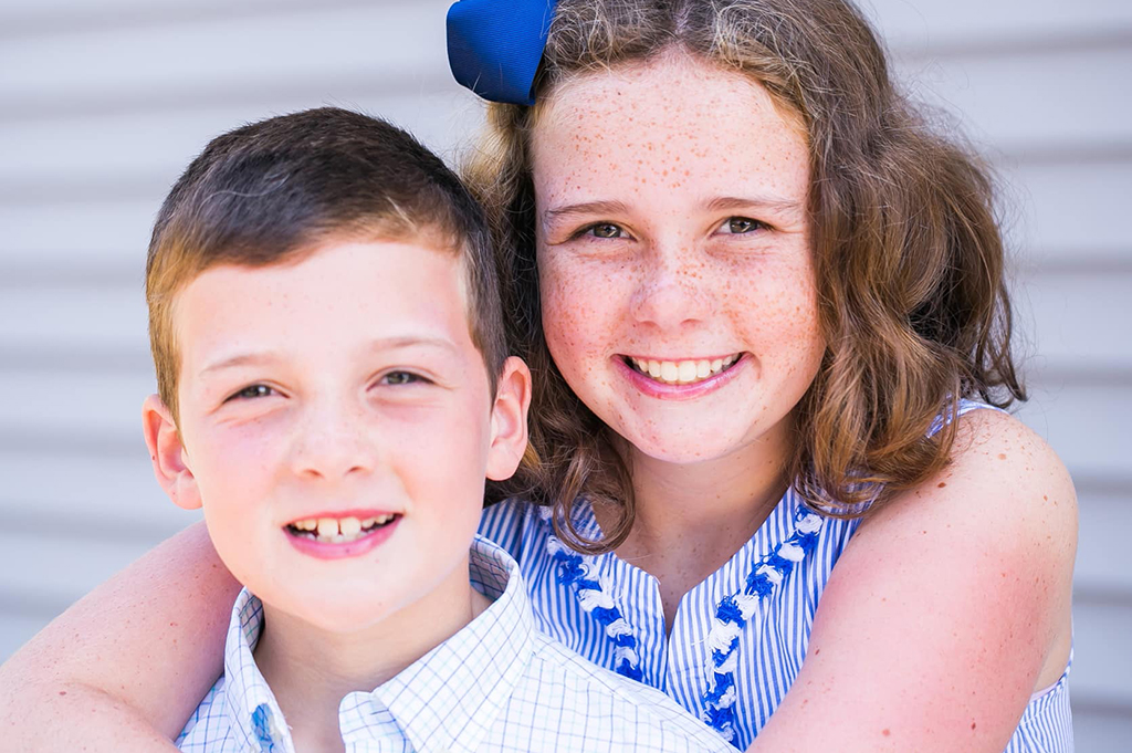 Sister holding onto her brother in blue and white on a warm summer day