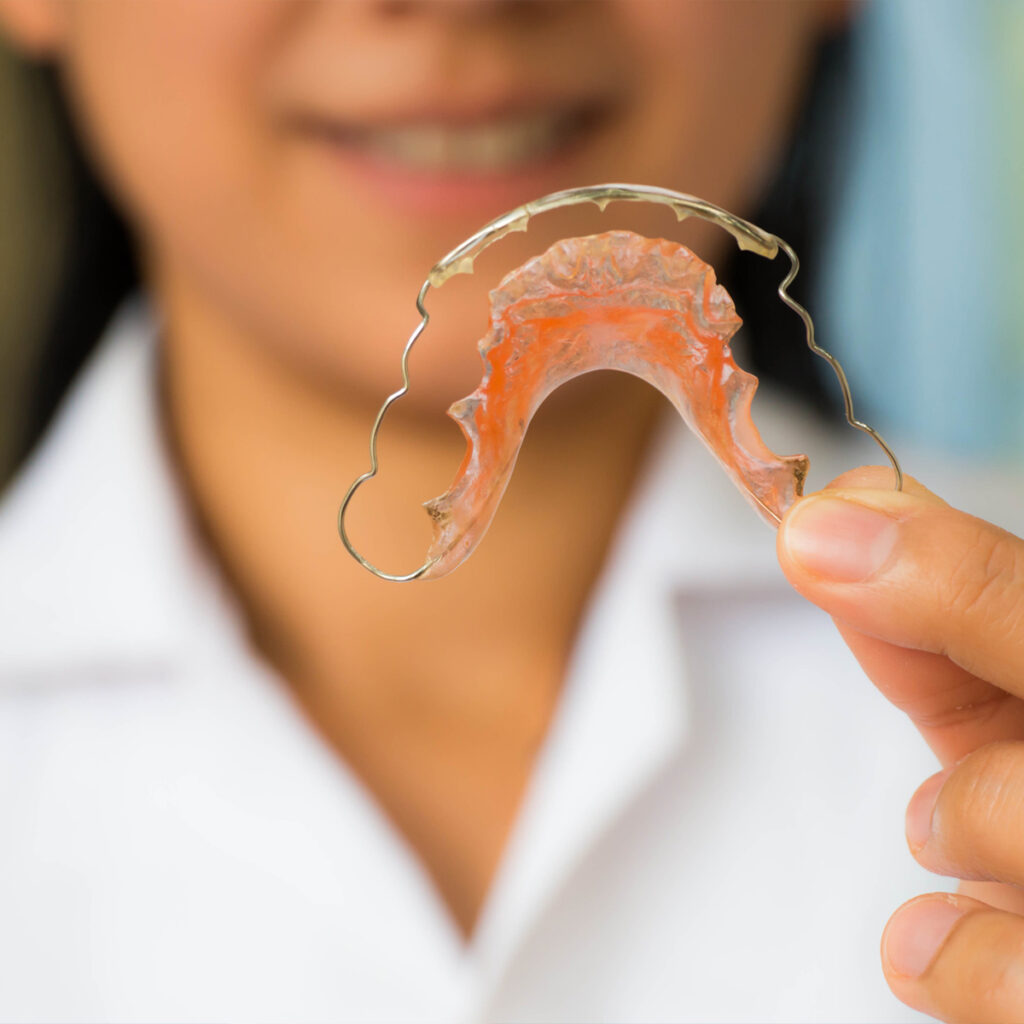 Orthodontist holding a removable metal retainer in front wearing a white shirt.