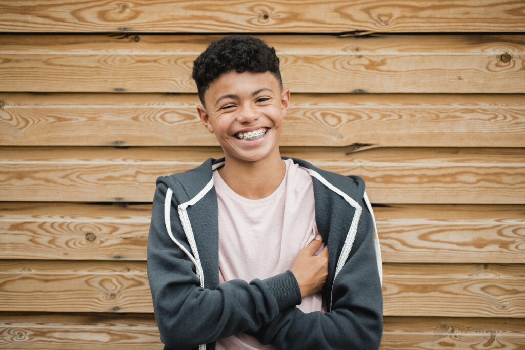 Teen with radiant smile and braces smiling in front of a wooden wall