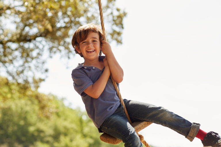 Young boy smiling while swinging on a rope and wood swing