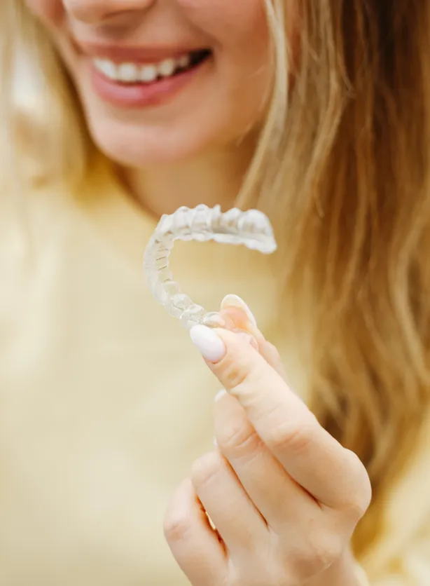 Young woman laughing while holding her clear aligner in her left hand