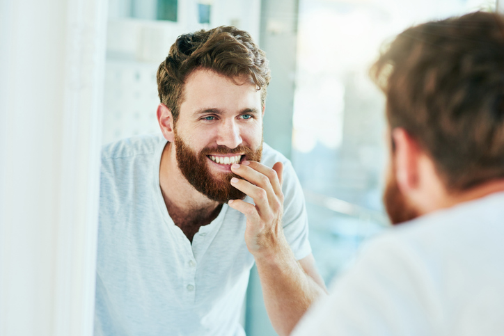 Photogenic man admiring his bright aligned smile in the mirror